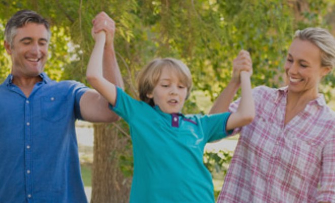 A boy playing with his parents in the park.