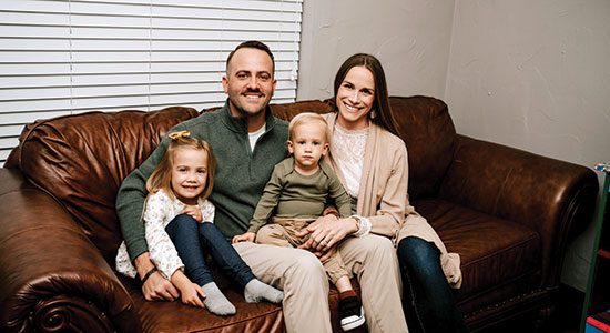 A young family, smiling and sitting together on the couch.