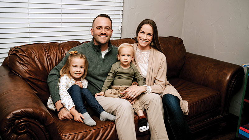 A young family, smiling and sitting together on the couch.